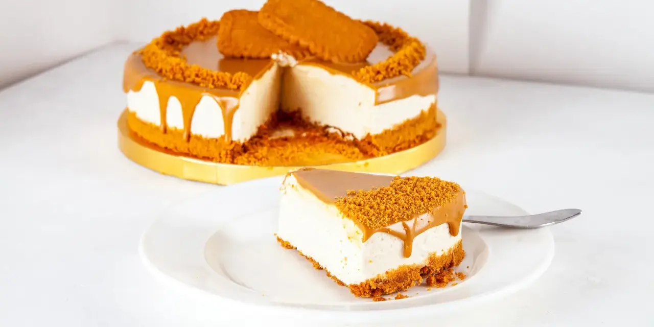 Ein cremiger Lotus Cheesecake mit Karamellglasuren und Keksbröseln. Ein Stück auf einem Teller, daneben ein ganzer Kuchen.