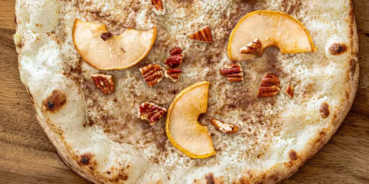 Eine süße Pizza mit dünnem Teig, bestreut mit Zimt, belegt mit Apfelscheiben und Pekannüssen. Ein Genuss wie eine Nutella Pizza!