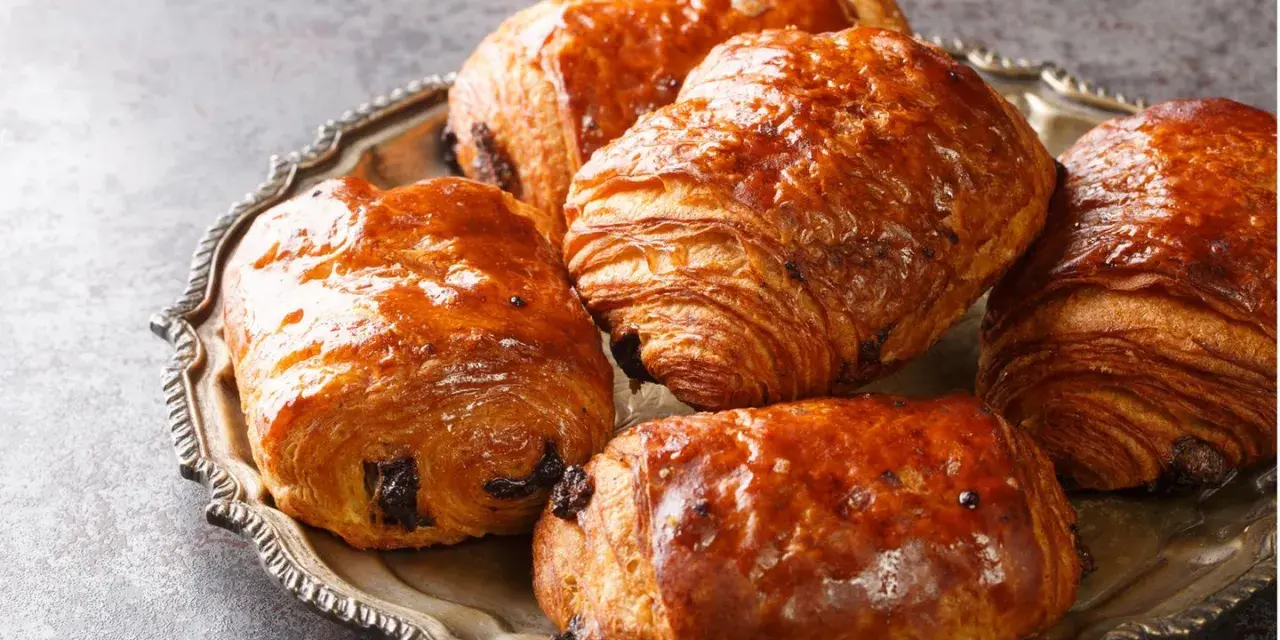 Einige goldbraune, knusprige Pain au Chocolat liegen auf einer silbernen Platte.