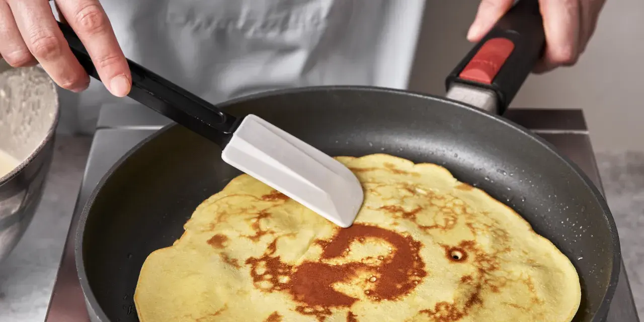 Ein goldbrauner Quark Pfannkuchen wird in einer Pfanne mit einem Spatel gewendet.