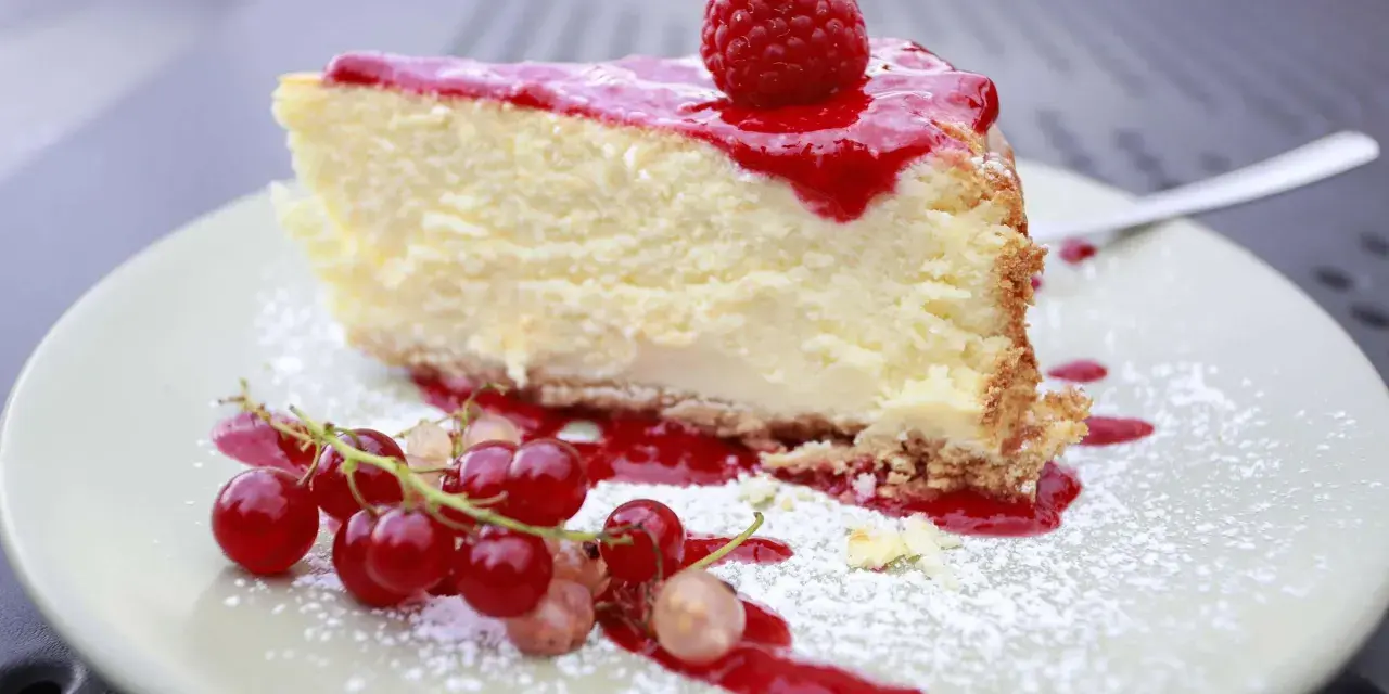 Ein Stück cremiger Käsekuchen mit Himbeersoße und frischen Beeren, bestäubt mit Puderzucker. Ein Genuss für alle Sinne, diese Himbeer Torte.