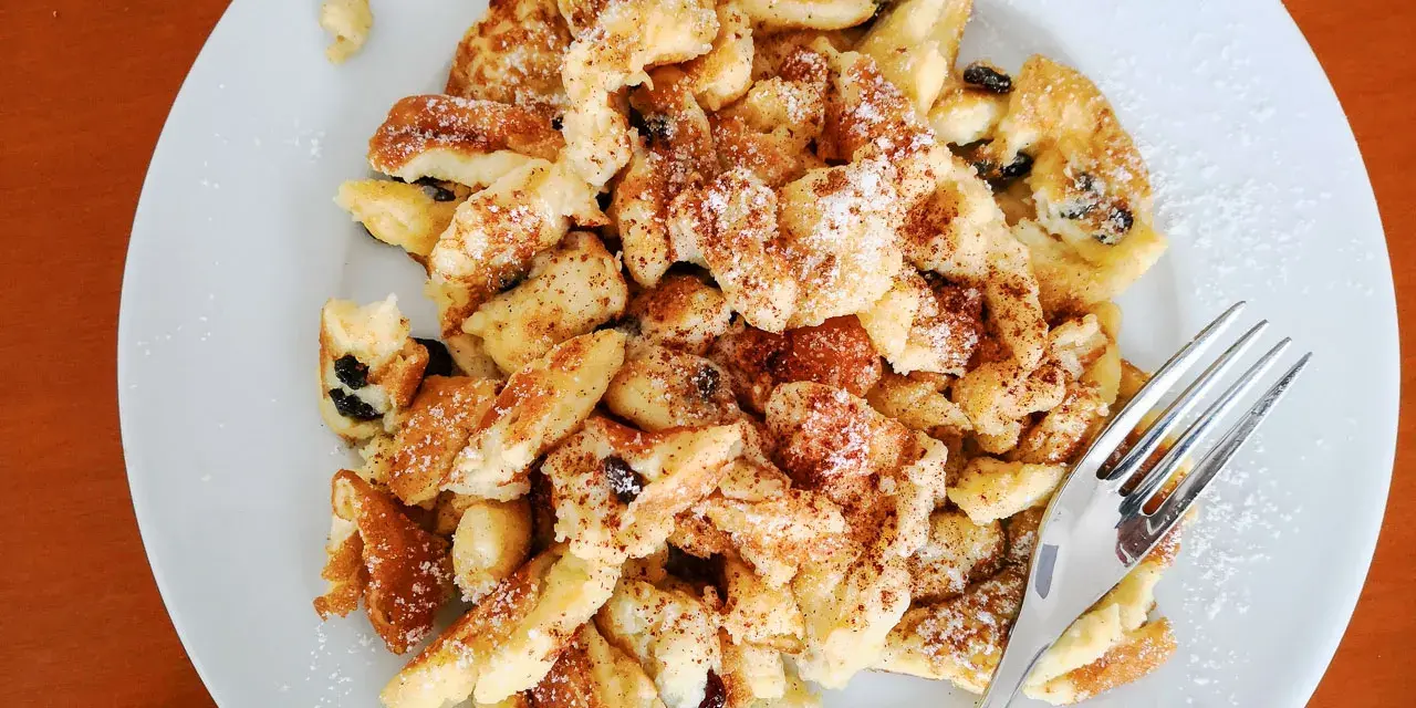 Ein Teller Kaiserschmarrn, bestreut mit Puderzucker und Zimt, wartet auf seine Verkostung. Dieses Kaiserschmarrn Rezept ist ein Klassiker.