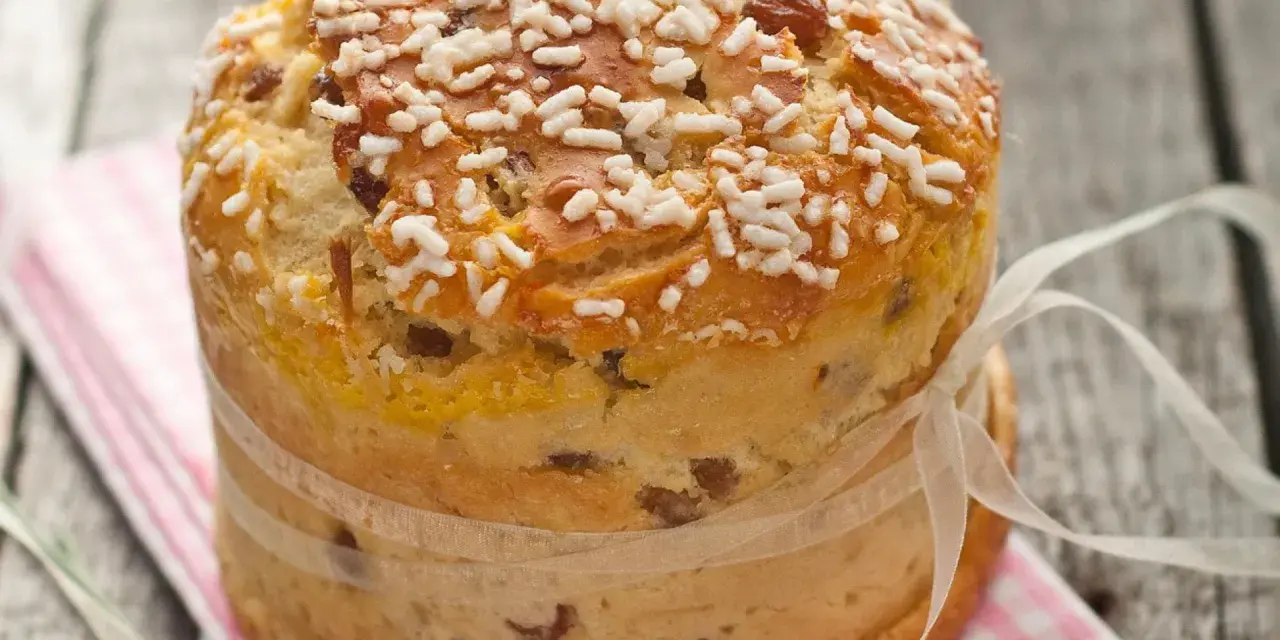 Ein goldbrauner Panettone mit Rosinen und Zuckerkristallen, gebunden mit einem Satinband. Ein köstliches Panettone Rezept zum Nachbacken.