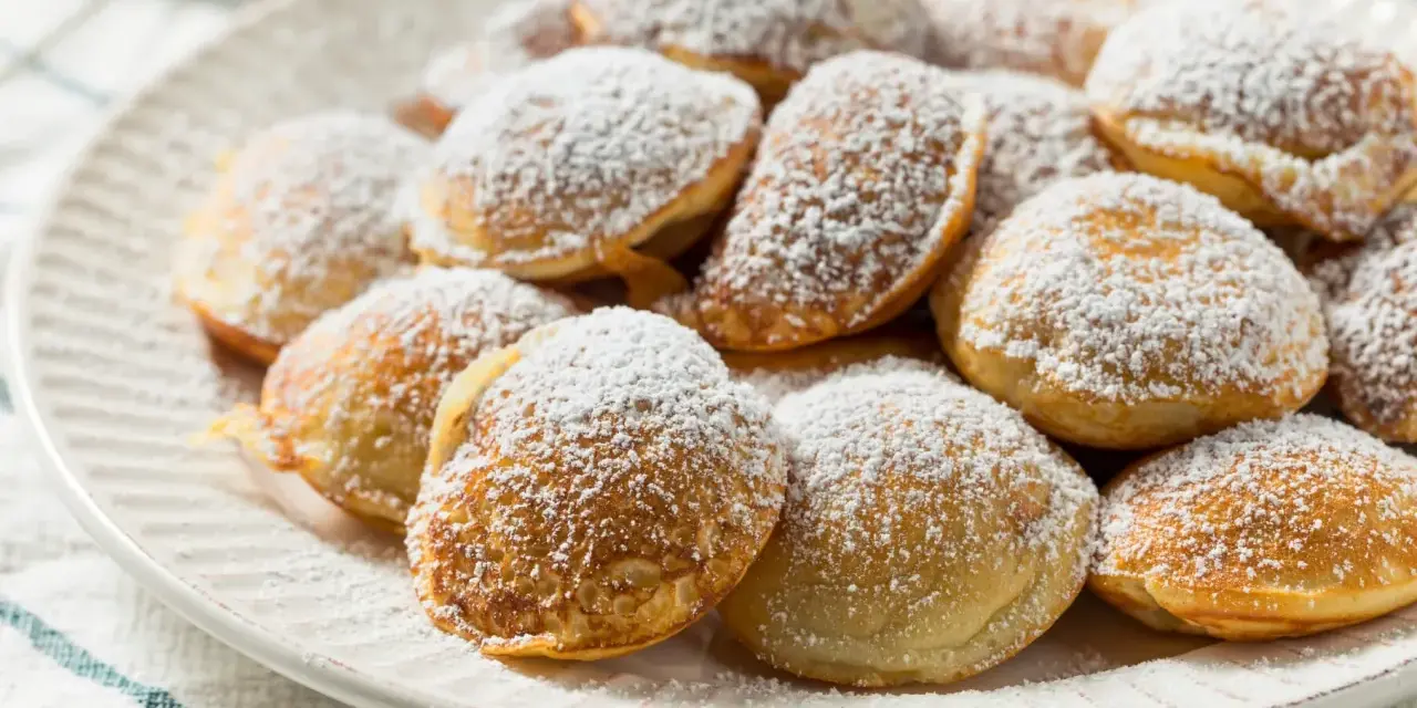 Ein Teller voller goldbrauner Poffertjes, bestäubt mit Puderzucker. Dieses Poffertjes Rezept ist ein Genuss!