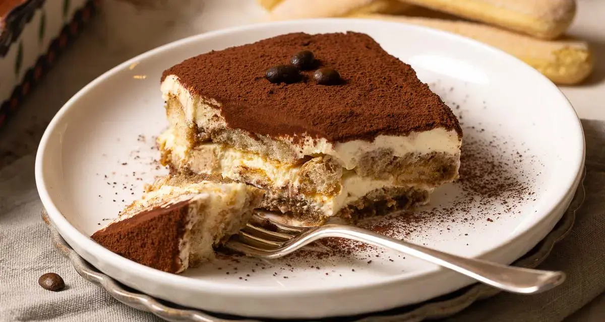 Ein Stück Tiramisu mit Kakaopulver bestäubt, bereit zum Genießen. Dieses klassische Tiramisu Rezept ist ein Genuss.