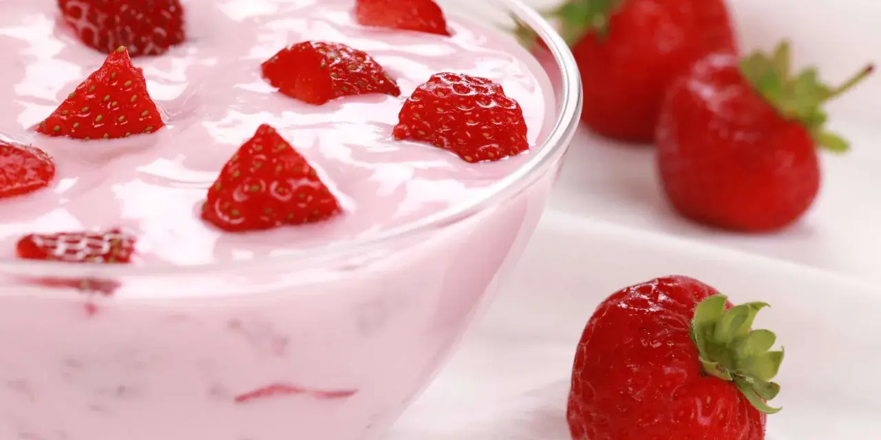 Ein cremiges Erdbeer Dessert in einer Schüssel, garniert mit frischen Erdbeerstücken. Daneben liegen ganze Erdbeeren.