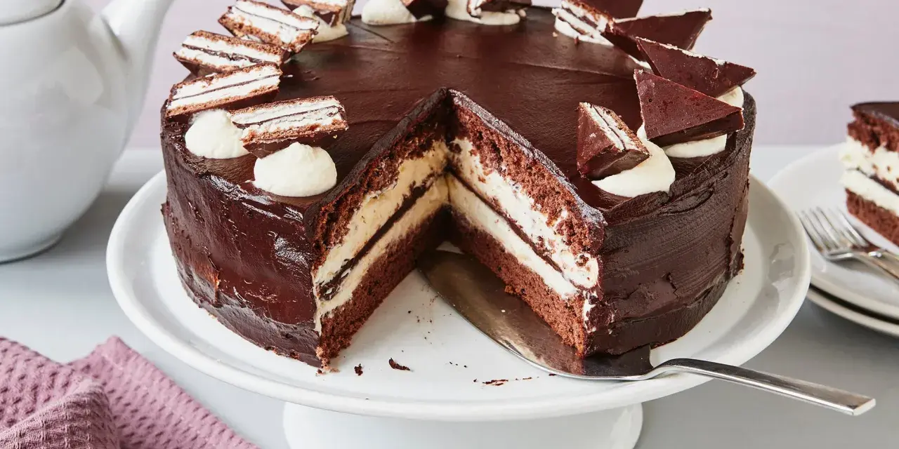 Eine köstliche Kinder Pingui Torte mit Schokoladenglasur, Sahnetupfern und kleinen Schoko-Biskuit-Stücken. Ein Stück ist bereits angeschnitten.