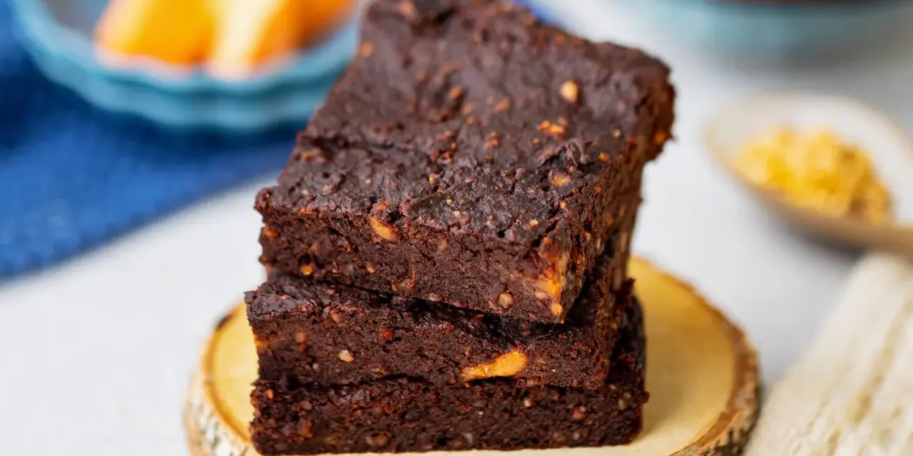 Gestapelte, saftige vegane Brownies mit Nüssen, auf einem Holzscheit.