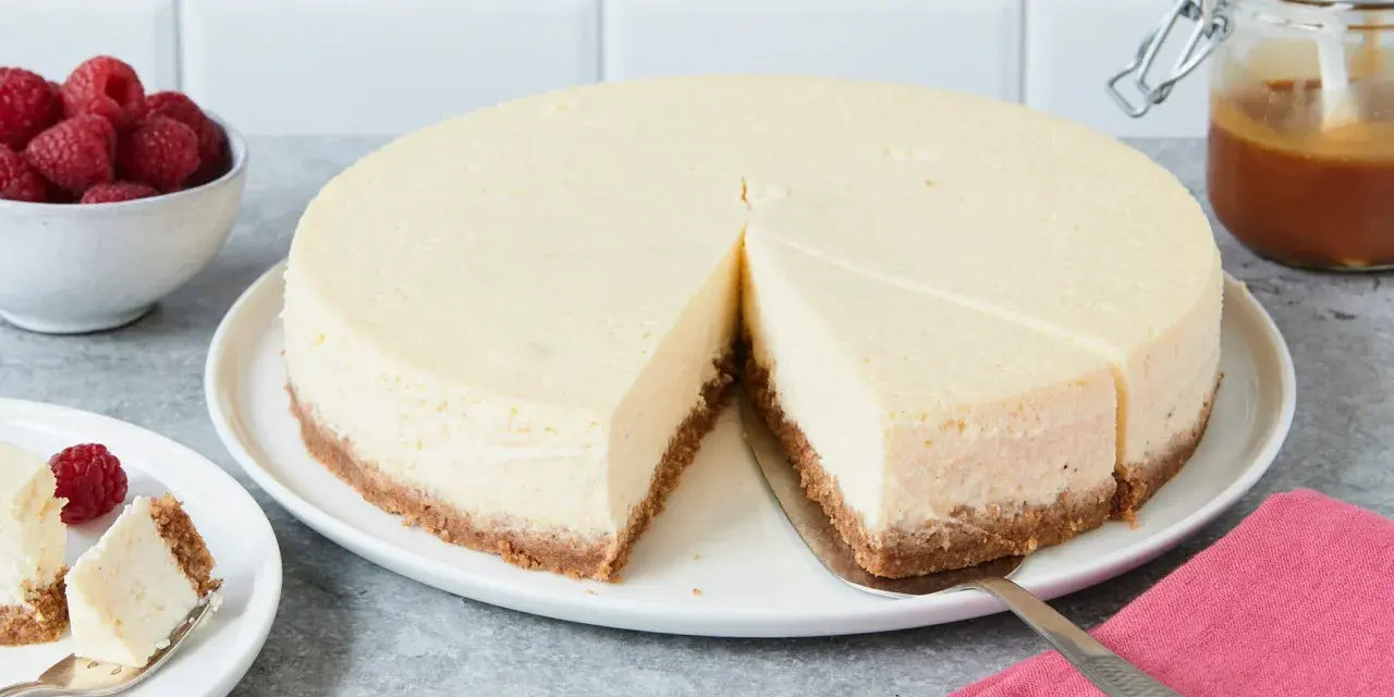Ein cremiger New York Cheesecake mit knusprigem Boden, garniert mit Himbeeren und Karamell.