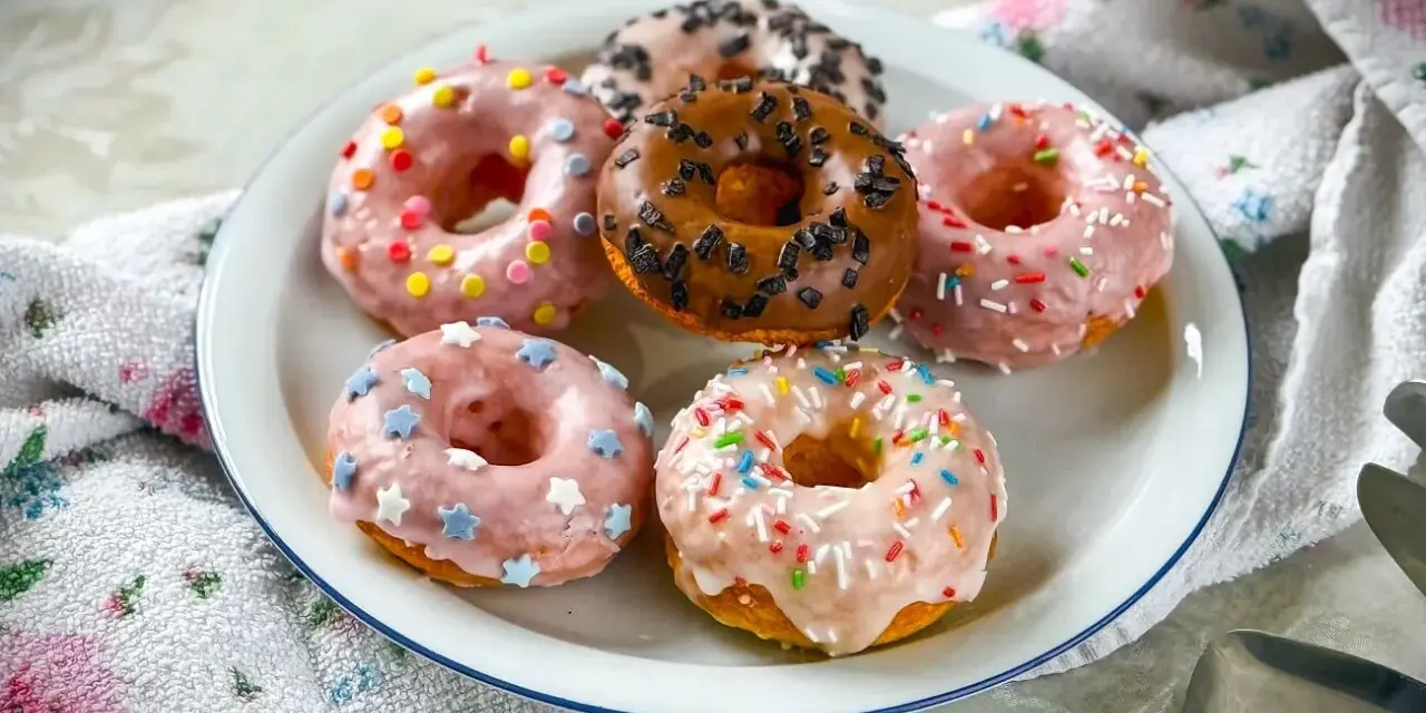 Sechs bunte Donuts auf einem Teller, perfekt für ein schnelles Donuts Rezept. Mit Streuseln und Sternen verziert.