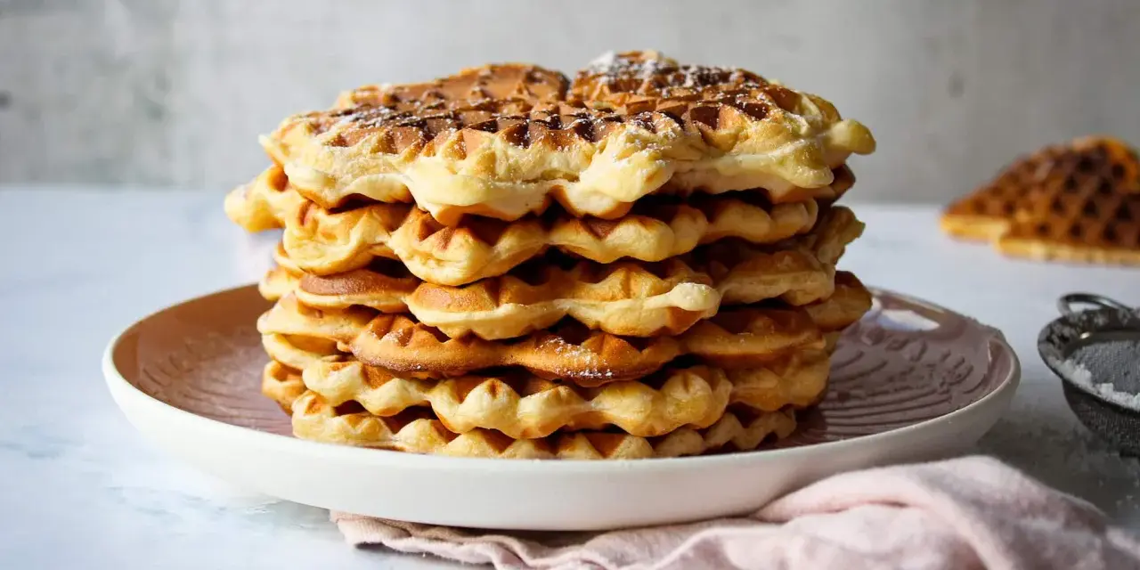 Ein Stapel goldbrauner Quarkwaffeln, bestäubt mit Puderzucker. Perfekt für ein schnelles Quarkwaffeln Rezept.