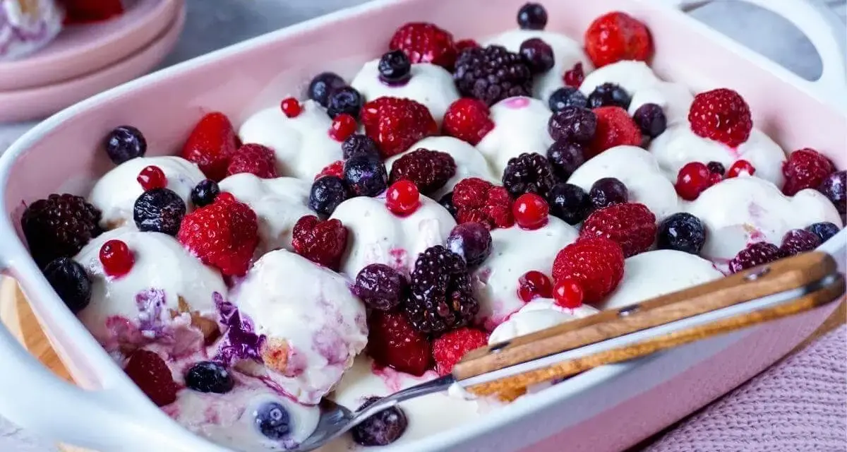 Ein cremiges Windbeutel-Dessert mit frischen Beeren wie Himbeeren, Brombeeren und Blaubeeren, serviert in einer rosa Schale.