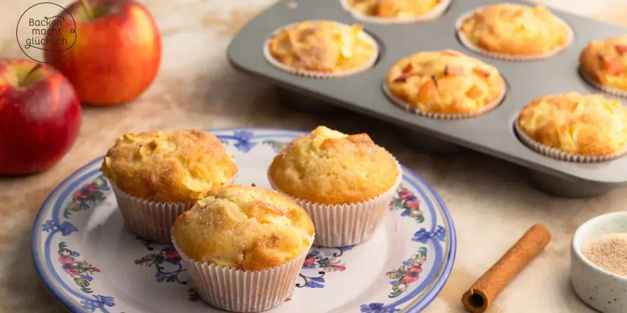 Frisch gebackene Apfelmus Muffins auf einem Teller, daneben Äpfel und Zimt.