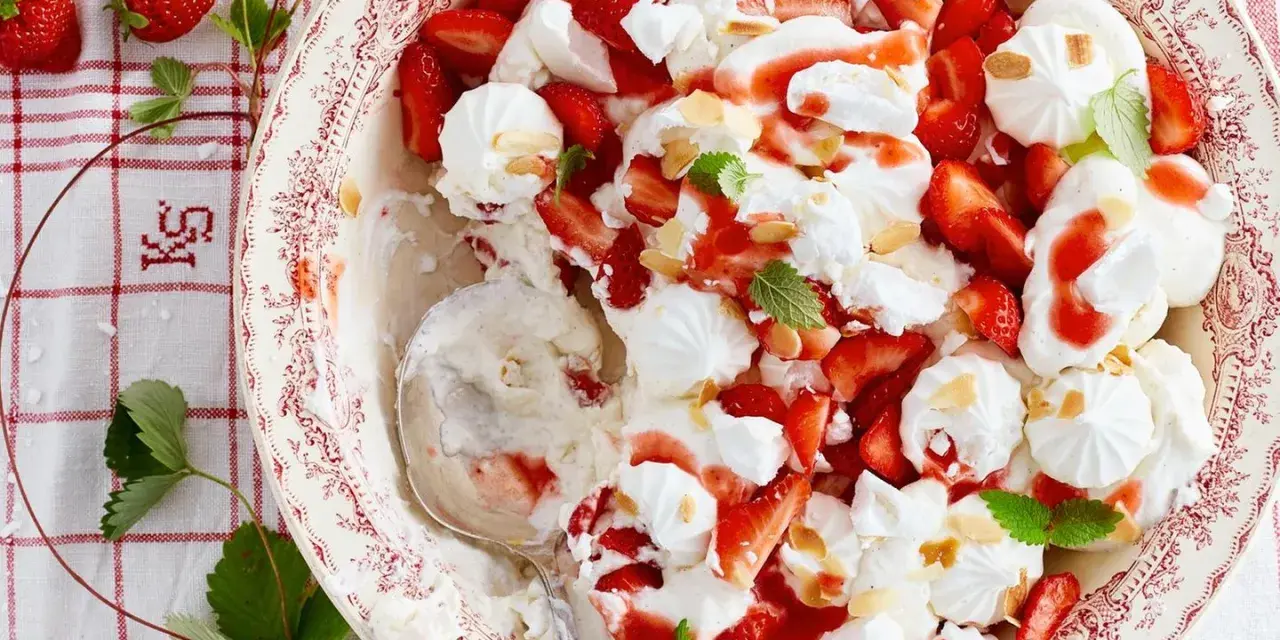 Ein köstlicher Eton Mess mit frischen Erdbeeren, Baiser und Sahne, garniert mit Mandelsplittern und Minze.