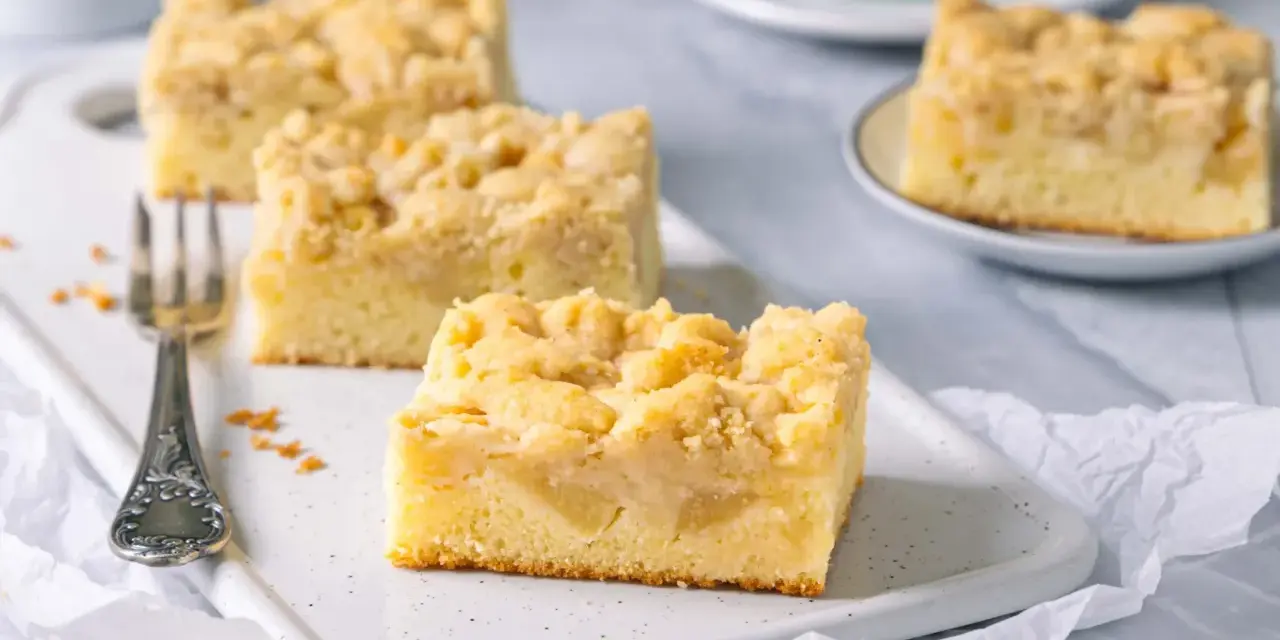 Saftiger Apfelkuchen mit Streuseln, perfekt für eine Kaffeepause. Ein Stück ist schon auf einer kleinen Platte angerichtet.