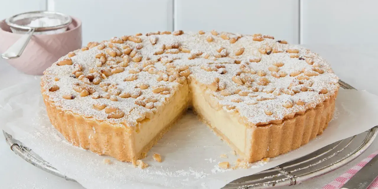 Eine köstliche Torta della Nonna, bestäubt mit Puderzucker und Pinienkernen, wartet darauf, angeschnitten zu werden.