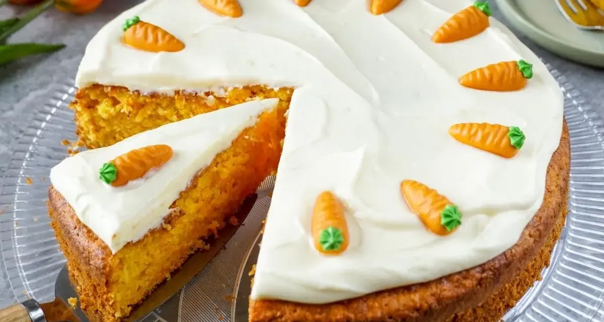 Saftiger Karottenkuchen mit cremigem Frosting und süßen Marzipan-Karotten. Ein Stück ist bereits angeschnitten.