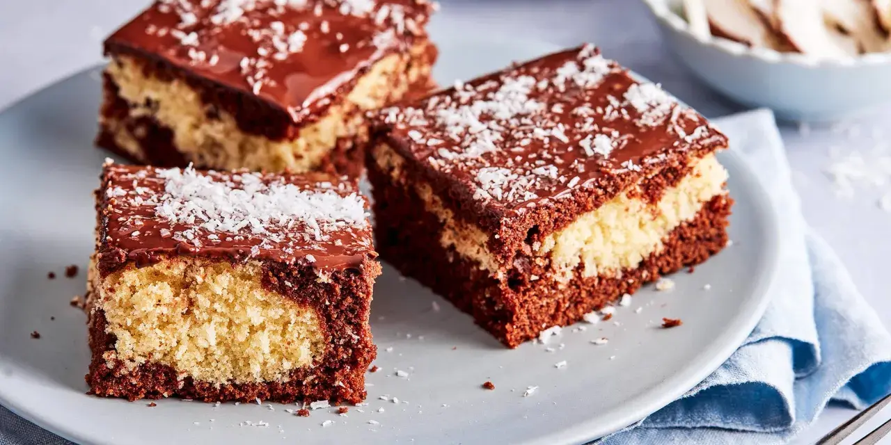 Drei Stücke saftiger Schoko Kokos Kuchen mit Schokoladenglasur und Kokosraspeln auf einem grauen Teller.