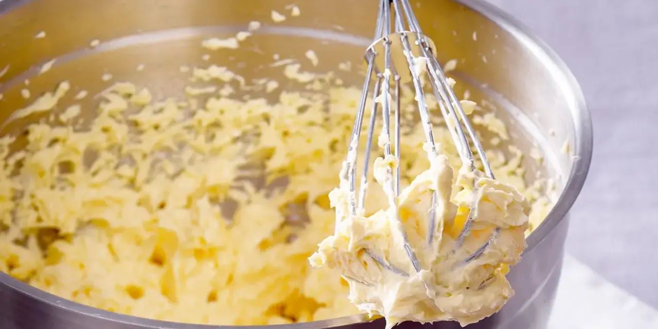 Ein Schneebesen mit cremigem Teig, bereit für ein Buttercreme Rezept.