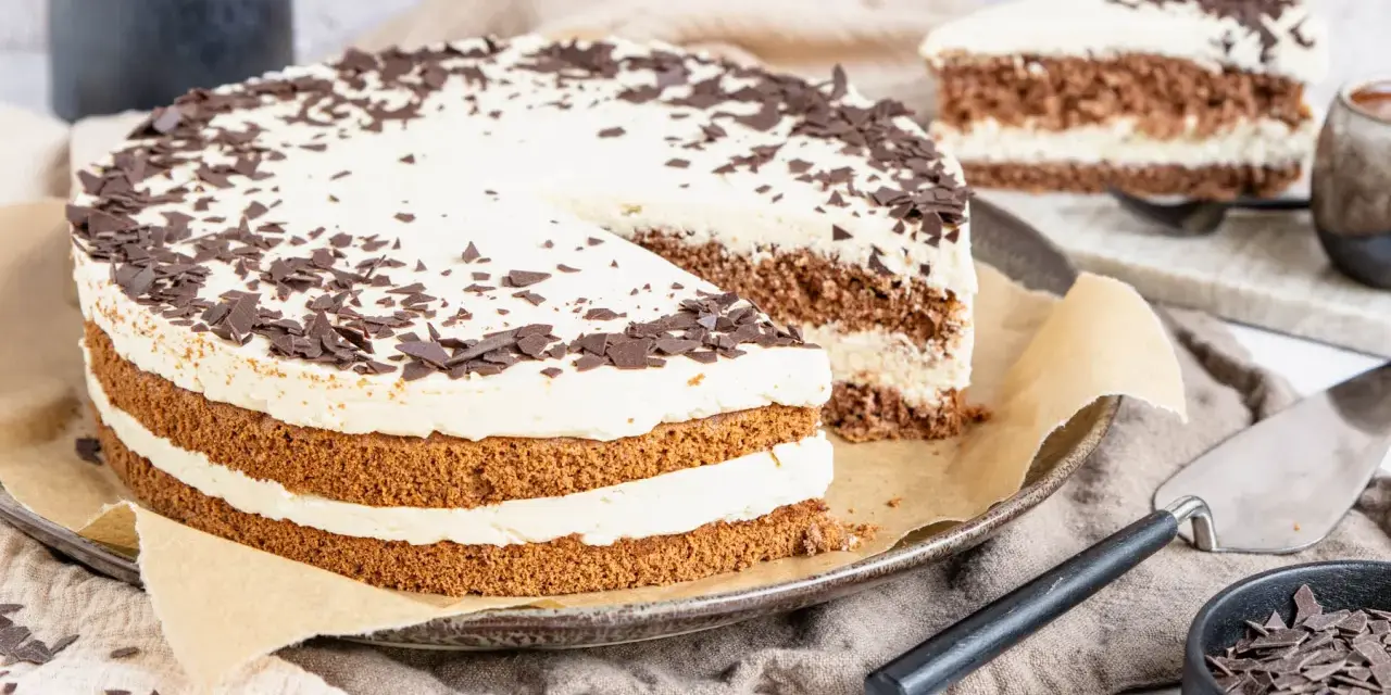 Eine köstliche Cappuccino Torte mit Schokoladenraspeln bestreut, auf einem Teller mit einem angeschnittenen Stück.