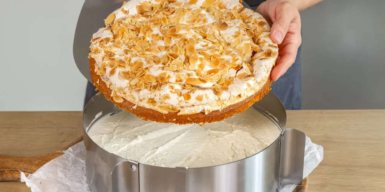 Eine köstliche Stachelbeer Baiser Torte mit Mandel-Topping wird gerade in einen Tortenring gesetzt.