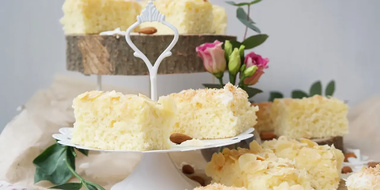 Saftige Buttermilchkuchenstücke mit Mandelsplittern und Kokosraspeln, garniert mit Blumen.