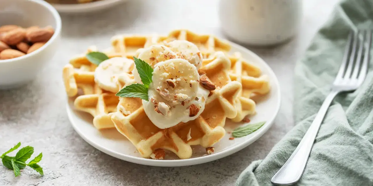 Goldbraune Skyr Waffeln mit Bananenscheiben, gehackten Mandeln und Minze. Ein köstlicher Start in den Tag!