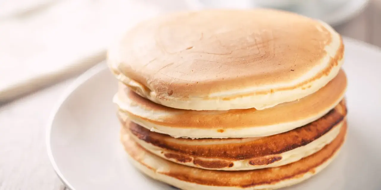 Ein Stapel goldbrauner, glutenfreier Pfannkuchen auf einem weißen Teller, bereit zum Genießen.