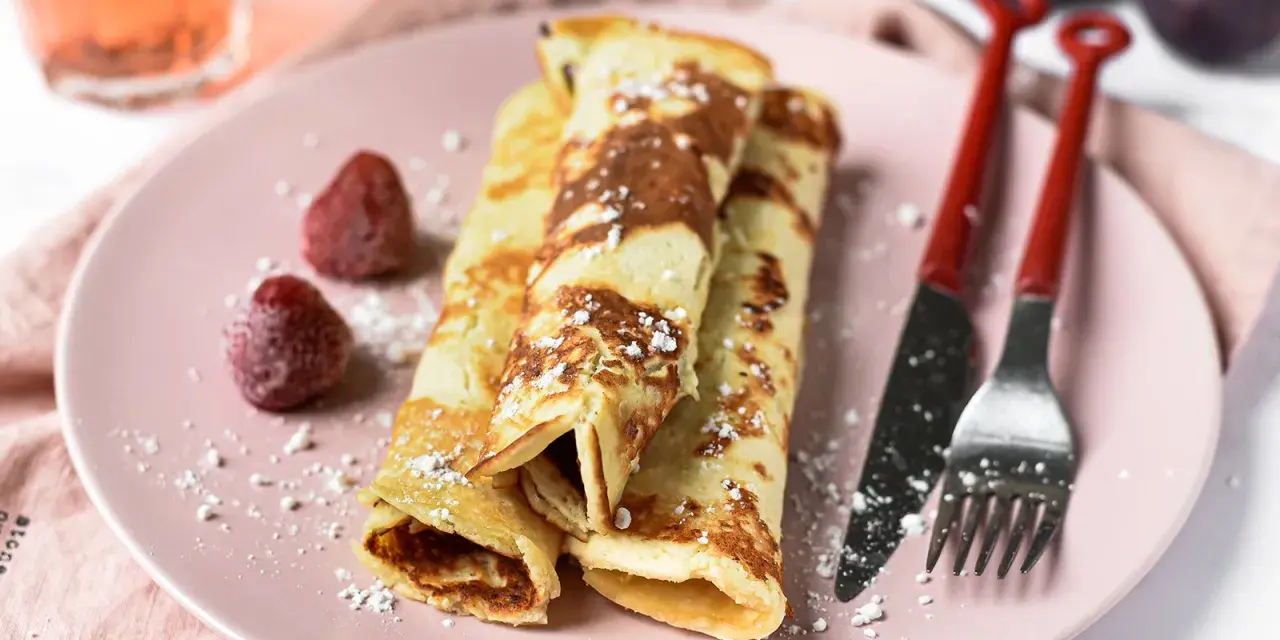 Gefüllte Pfannkuchen ohne Mehl, bestäubt mit Puderzucker, serviert mit Erdbeeren und Feigen.