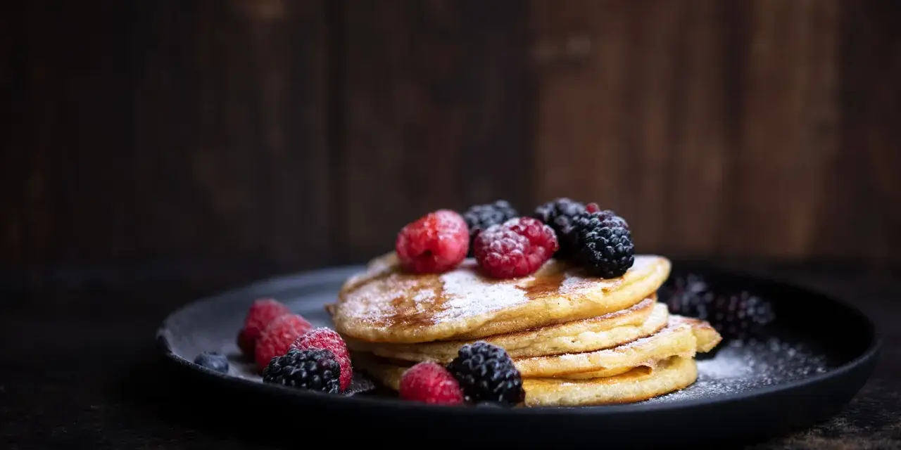 Stapel goldbrauner Pancakes, bestäubt mit Puderzucker und garniert mit frischen Himbeeren und Brombeeren. Ein köstliches Pancakes Rezept für jeden Anlass.