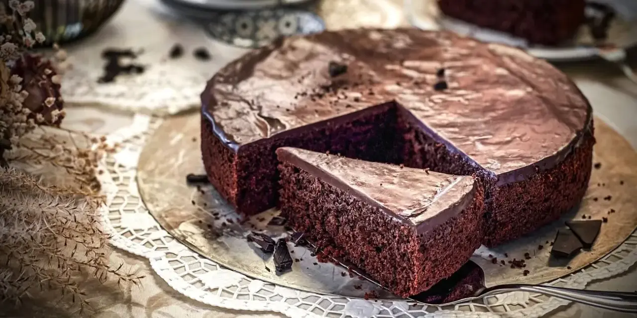 Ein saftiger, schneller Schokokuchen mit glänzender Glasur und einer Kuchenscheibe auf einem Tortenheber.