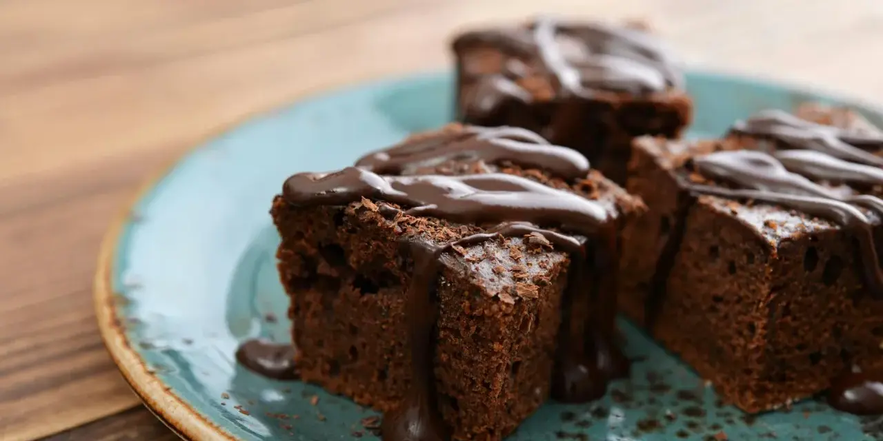 Saftige Brownies, perfekt für ein schnelles Brownie Rezept. Mit flüssiger Schokolade übergossen und auf einem türkisfarbenen Teller angerichtet.