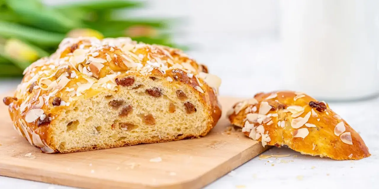 Ein goldbraunes Osterbrot mit Mandelsplittern und Rosinen, perfekt für Ihr Osterbrot Rezept. Daneben ein Stück des süßen Gebäcks.