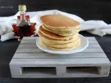 Ein Stapel goldbrauner Pfannkuchen, bereit für ein köstliches Frühstück. Daneben eine kleine Flasche Ahornsirup. Ein einfaches Pfannkuchen Rezept für jeden Tag.
