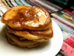 Ein Stapel goldbrauner Pancakes mit Kefir, beträufelt mit Honig, auf einem weißen Teller.