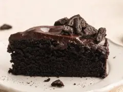 Ein saftiges Stück dunkler Oreo Kuchen mit glänzender Schokoladenglasur und zerbröselten Keksen obendrauf.