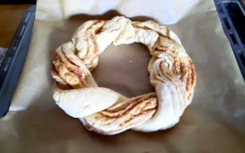 Ein geflochtener Teigring mit Zimtfüllung liegt auf Backpapier. Perfekt für das Osterkranz backen.