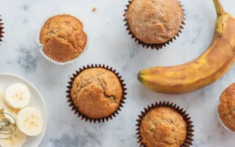 Leckere Bananen Muffins, frisch gebacken, mit einer reifen Banane und Bananenscheiben daneben.