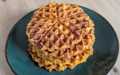Ein Stapel goldbrauner Haferflocken Waffeln auf einem dunklen Teller. Sie sehen knusprig und lecker aus, perfekt für ein gesundes Frühstück.