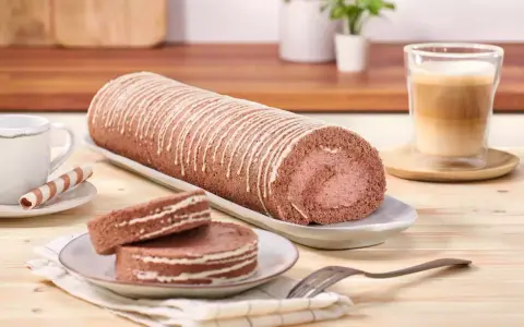 Eine köstliche schoko biskuitrolle mit weißer Glasur, dane zwei Scheiben und ein Kaffee.