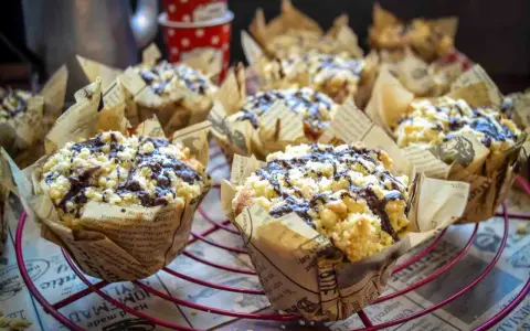 Saftige Nutella Muffins mit Streuseln und Schokoglasur, verpackt in Zeitungspapier-Förmchen, auf einem roten Gitter.