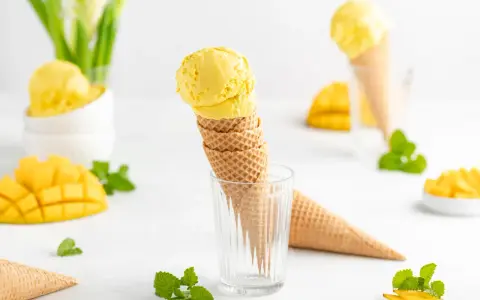 Ein Stapel Waffelkegel mit cremigem Mango Eis, garniert mit frischer Minze und Mangostücken. Ein süßer Genuss!