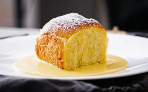 Ein goldbraunes Buchtel, mit Puderzucker bestäubt, ruht in einer cremigen Vanillesauce. Ein köstliches Buchtel Rezept zum Nachbacken.