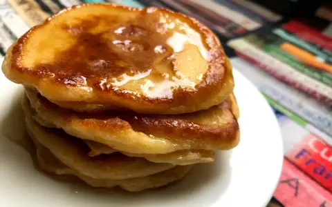 Ein Stapel goldbrauner Pancakes mit Kefir, beträufelt mit Honig, auf einem weißen Teller.