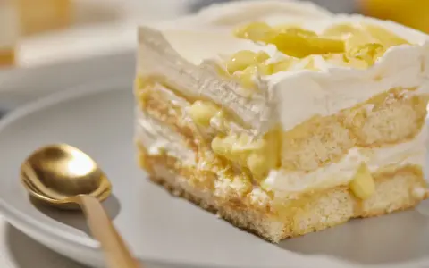Ein Stück Zitronen Tiramisu mit cremiger Füllung und Zitronenscheiben, daneben eine goldene Löffel.