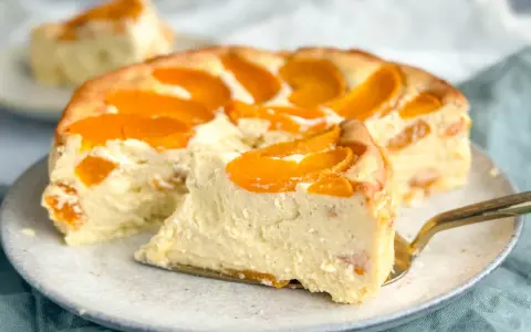 Ein saftiger Pfirsichkuchen mit cremiger Füllung und frischen Pfirsichspalten. Ein Stück wird gerade mit einem goldenen Tortenheber herausgehoben.