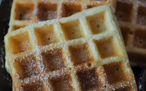 Goldbraune Waffeln, bestäubt mit Puderzucker, warten auf Joghurt. Ein süßer Genuss!