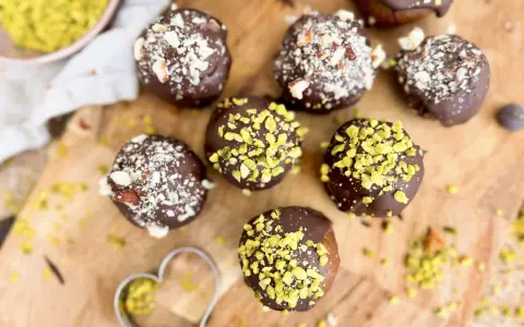 Selbstgemachte Pralinen mit Schokolade und gehackten Nüssen, einige mit Pistazien bestreut. Ein Herz-Ausstecher liegt daneben.
