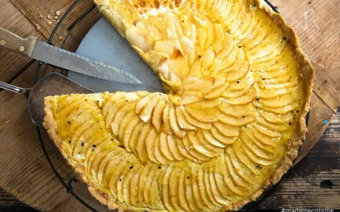 Ein köstliches Apfeltarte Rezept mit dünn geschnittenen Äpfeln, die wie Fächer angeordnet sind. Ein Stück wurde bereits herausgeschnitten.