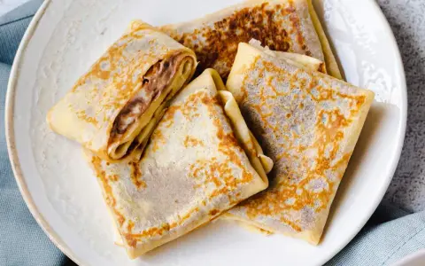 Gefaltete Crêpes mit Schokoladencreme-Füllung, ein köstliches Crepes Rezept, liegen auf einem Teller.